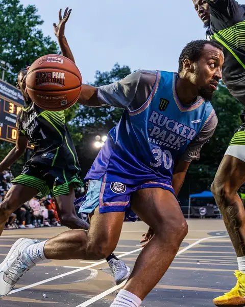 Player in a blue and purple Rucker Park number 30 jersey driving to the basket