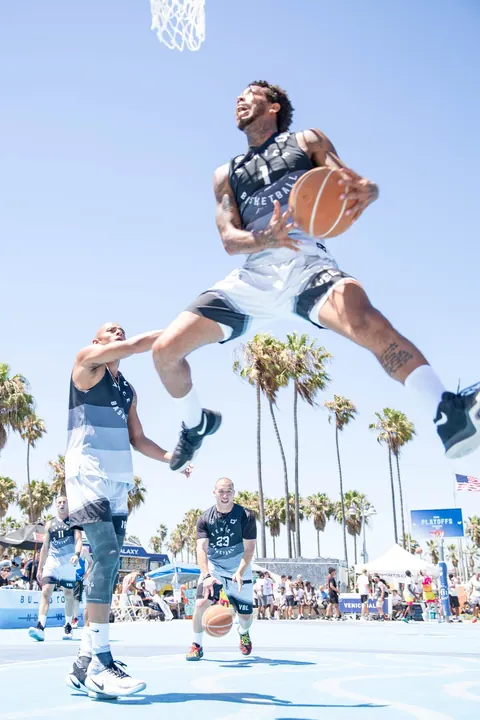 A Veniceball player in black and white soaring beneath the basket on the Venice Beach court