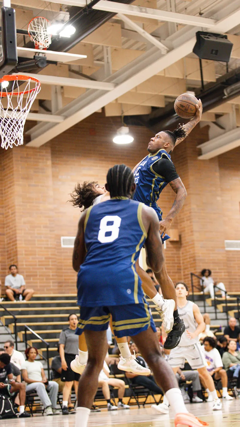 Drew League player in a navy number 8 uniform watching a teammate dunk